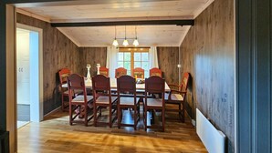 Een eetkamer met een houten tafel en stoelen, een raam met gordijnen en een plafond met zichtbare balken.