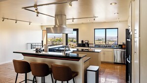 A modern kitchen with a central island, bar stools, stainless steel appliances, and large windows offering a view of the landscape. - Large Cozy Estate w/ VIEWS! 5 Min to Downtown (Paso Robles)