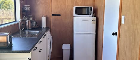 Et lille køkken med vask, brødrister, elkedel og mikrobølgeovn på et hvidt køleskab.