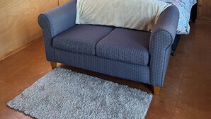 A bedroom with a wooden paneled wall, a bed with a floral bedspread, two bedside tables with lamps, and a blue sofa with a patterned cover.