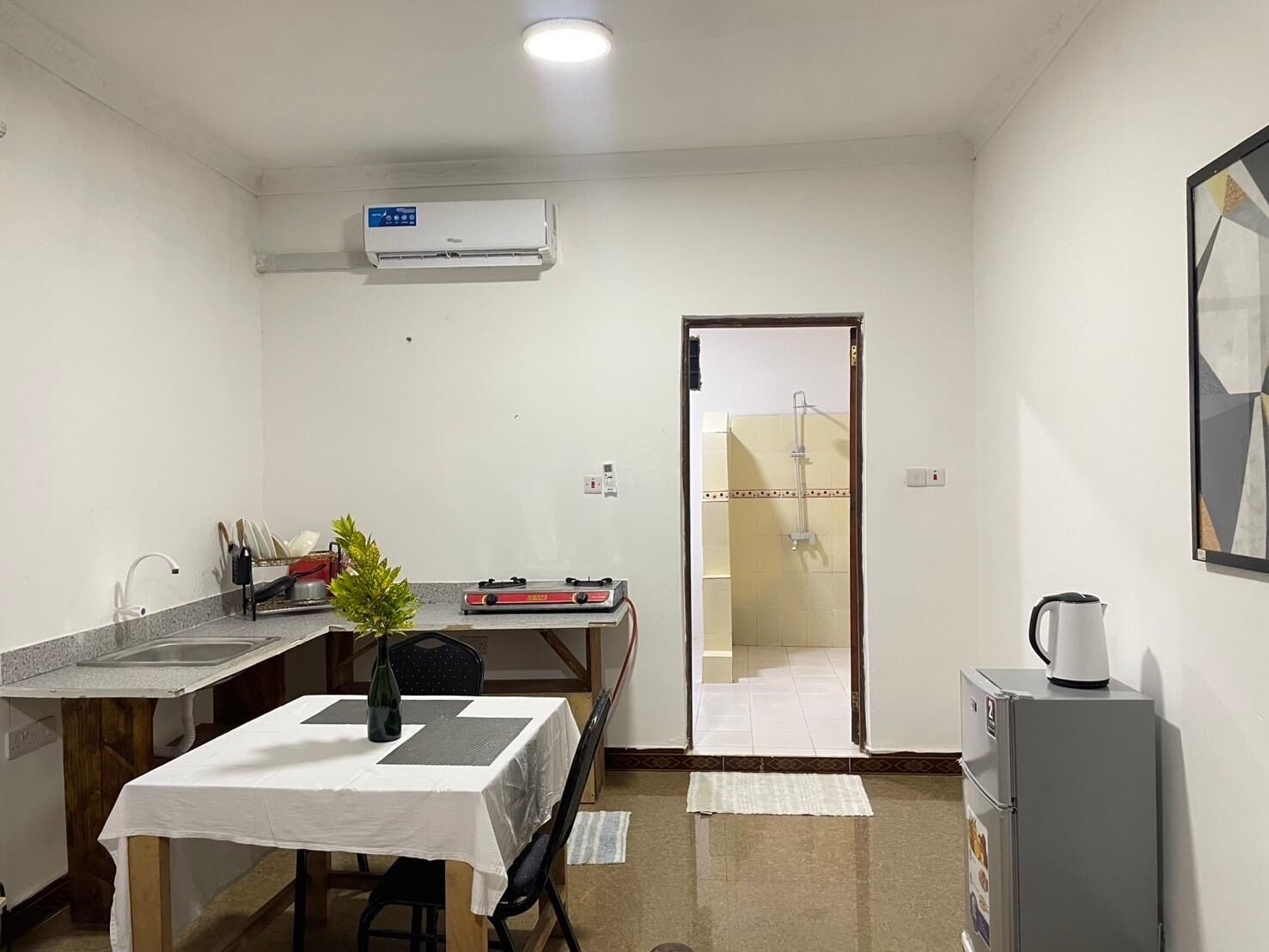 Een compacte keuken met een eettafel, een kleine koelkast, een spoelbak en een airconditioner.
