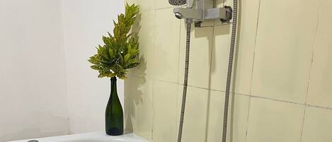 Una bañera blanca con un cabezal de ducha manual, una pequeña planta verde y un borde de azulejos decorativos en la pared.