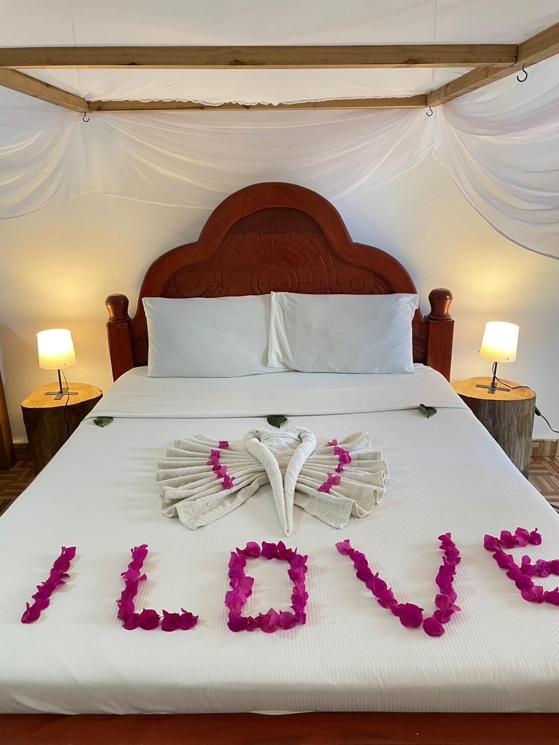 Una cama bien hecha con una toalla dispuesta en forma de corazón y la palabra “LOVE” escrita con pétalos de rosa.