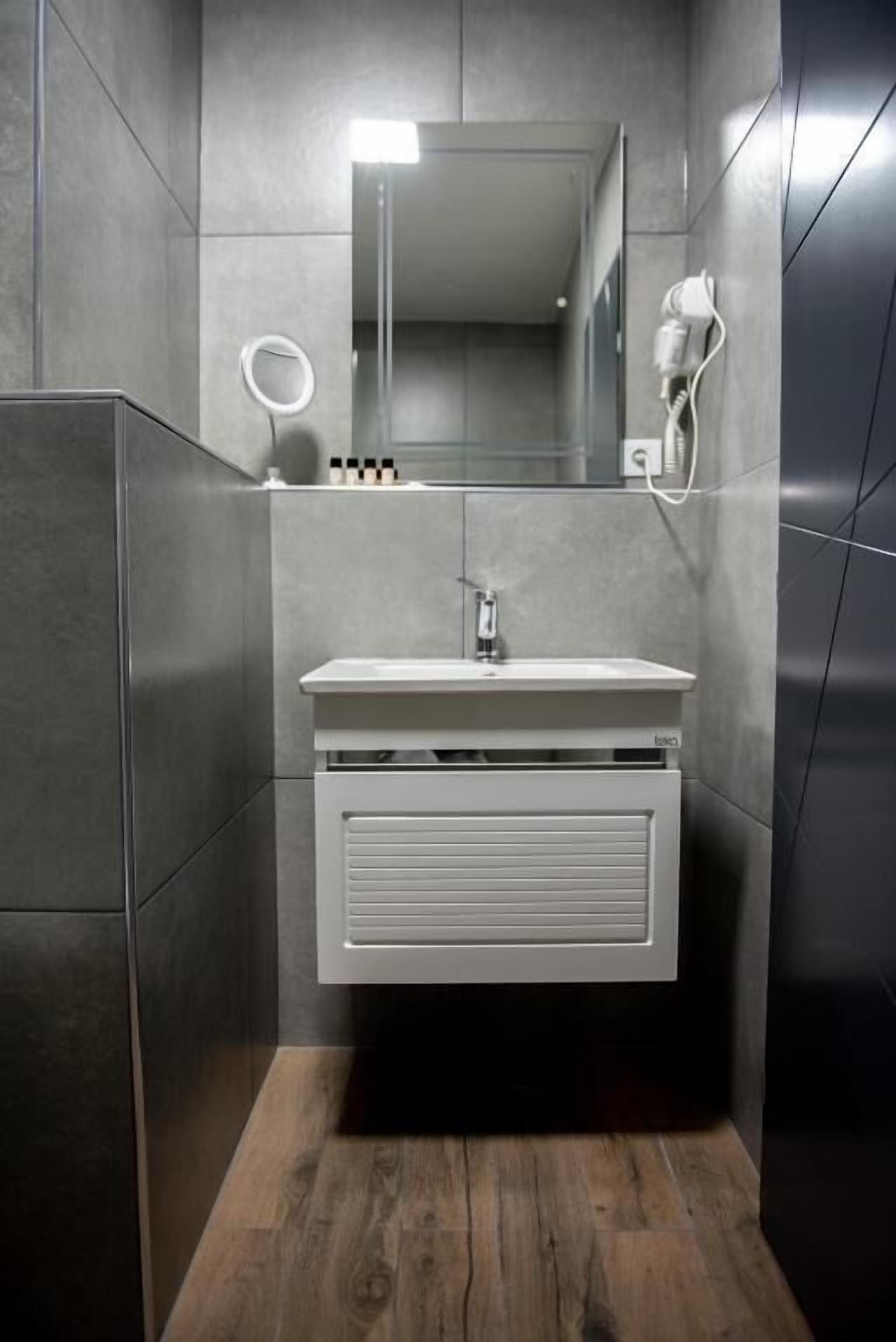 Un baño moderno con un tocador blanco, un espejo y un secador de pelo en la pared.