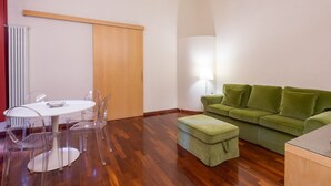 A room with a wooden floor, a green sofa, a white table with chairs, and a lamp.