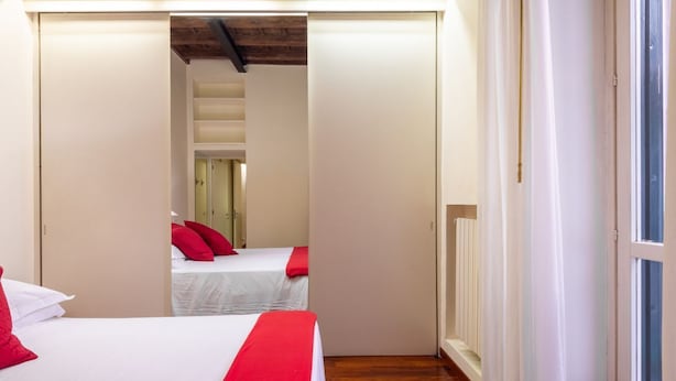 A hotel room with two beds, a wooden floor, and a view through an open door.