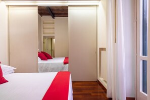Une chambre d’hôtel avec deux lits, un plancher en bois et une vue sur l’extérieur, visible à travers une porte ouverte.