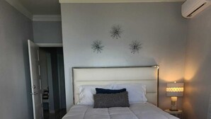 A bedroom with a large bed, a bedside table with a lamp, and decorative wall sconces. - New 3-bed oceanview villa, Black Point, Exuma near Staniel, AC, Wifi dock access (Black Point Exuma)