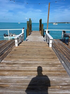 A wooden pier leading to a dock with boats, a clear sky, and a shadow of a person. - New 3-bed oceanview villa, Black Point, Exuma near Staniel, AC, Wifi boat access (Black Point Exuma)