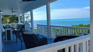 A covered outdoor seating area with a view of the ocean, featuring ceiling fans and a white railing. - New 3-bed oceanview villa, Black Point, Exuma near Staniel, AC, Wifi dock access (Black Point Exuma)