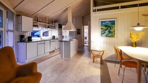 Cozinha moderna com armários brancos, ilha central e iluminação pendente. Há um espaço de refeições com mesa e cadeiras, e um quadro na parede.