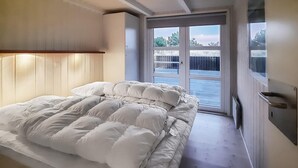 Quarto com uma cama grande, cabeceira de madeira e porta de vidro deslizante que dá para uma varanda.