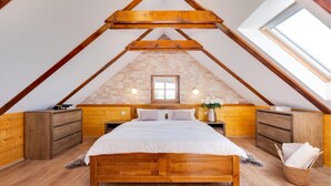 Une chambre avec un plafond en pente, des poutres apparentes, un mur en briques, un lit en bois, des tables de chevet et une fenêtre.