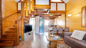 Un intérieur en bois avec un escalier, un espace de vie comprenant un canapé et une table basse, et une cuisine avec une table à manger.