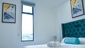 A hotel room with a bed, a window, and two framed artworks on the walls.