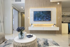 A modern living room with a round coffee table, a vase with flowers, a painting on the wall, and a built-in bench with a light underneath. - Exclusive High-Floor 2BR Aykon with Luxury & Views (Dubai)