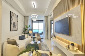 A modern living room with a sofa, coffee table, and TV. There is a large window and a plant. - Exclusive High-Floor 2BR Aykon with Luxury & Views (Dubai)
