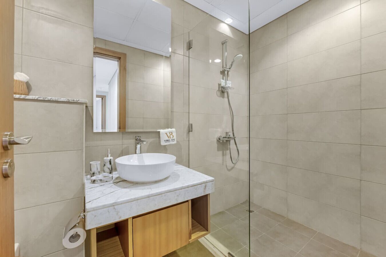 A modern bathroom with a large white sink, a glass-enclosed shower, and a wooden cabinet below the sink.