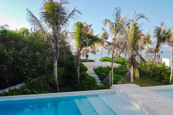 Área da piscina com vista para o mar, cercada por palmeiras e um caminho que leva à praia.
