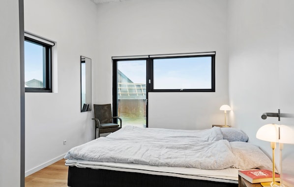 A bedroom with a bed, a chair, a desk with a lamp, and a window.