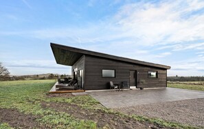 Een modern huis met een schuin dak, een terras met tuinmeubilair en uitzicht op het omliggende landschap.