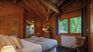 A cozy wooden cabin bedroom with a bed, a chair, a dresser, and a window with a view of greenery. - Chalet Chavanette - spacious holiday home for 12 with spa - OVO Network (La Chapelle-d'Abondance)