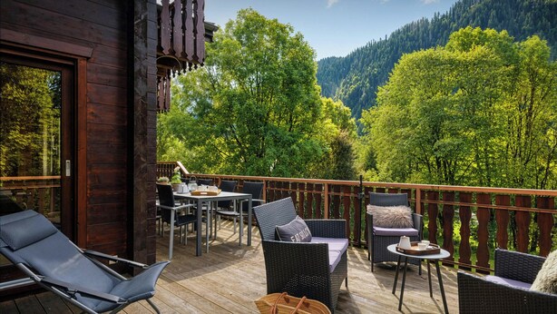 A wooden deck with wicker furniture, a table, and chairs. - Chalet Chavanette - spacious holiday home for 12 with spa - OVO Network (La Chapelle-d'Abondance)