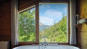 A bathroom with a bathtub, a toilet, and a window offering a view of a forest and mountains. - Chalet Chavanette - spacious holiday home for 12 with spa - OVO Network (La Chapelle-d'Abondance)