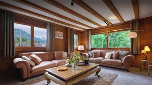 A cozy living room with a wooden ceiling, two sofas, a coffee table, and large windows offering a view of greenery and mountains. - Chalet Chavanette - spacious holiday home for 12 with spa - OVO Network (La Chapelle-d'Abondance)