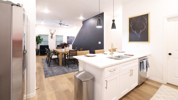 Eine moderne Küche mit weißen Schränken, einer zentralen Kochinsel mit Spüle, Pendelleuchten und einem Deckenventilator.