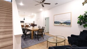 Un salon moderne avec un canapé bleu foncé, une table basse en verre et un coin repas comprenant une table et des chaises en bois.
