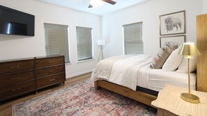 Une chambre à coucher comprenant un lit, une commode, un ventilateur de plafond, un téléviseur fixé au mur et des œuvres d’art.