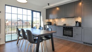 Une cuisine moderne avec des meubles gris, une table à manger en bois avec des chaises, et une grande fenêtre donnant sur les bâtiments environnants.