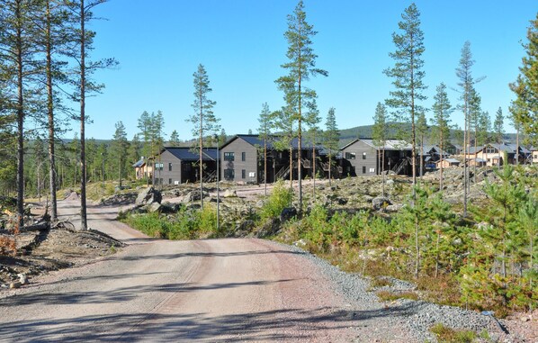 Une cabane en rondins moderne, avec une allée en gravier menant à une terrasse en bois.