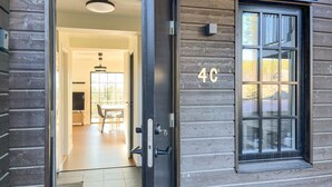 Une façade en bois avec une porte vitrée donnant sur un intérieur comprenant un coin repas et une grande fenêtre.