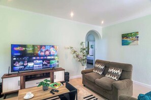 Una sala de estar con una televisión de pantalla plana, un sofá marrón, una mesa de centro y una planta.