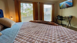A bedroom with a bed, a desk, a chair, a TV, and a window with curtains.