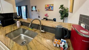 A kitchen with a granite countertop, stainless steel sink, and a red Keurig coffee maker.