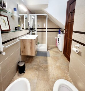 Un baño moderno con tocador de madera, cabina de ducha de vidrio, lavadora y dos inodoros.