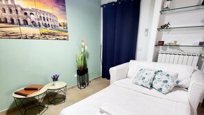 A hotel room with a bed, a small table with a chair, a wall-mounted air conditioner, and a shelf with decorative items. - Villetta Alessandra Ostia Antica 10 mins from beach (Lazio)