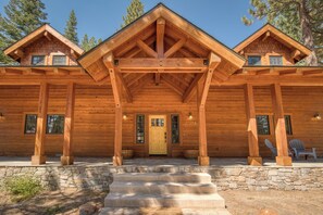 Une cabane en rondins avec des fondations en pierre, une véranda en bois et deux cheminées.