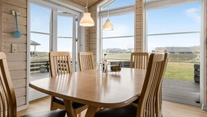 Une table à manger en bois, avec six chaises, de grandes fenêtres et une vue sur l’extérieur.