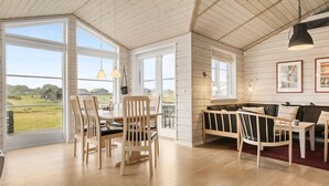 Une pièce spacieuse avec de grandes fenêtres, une table à manger en bois et un coin salon confortable avec un canapé et des fauteuils.