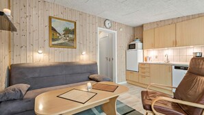Tunnelmallinen huone, jossa on puuseinä, sohva, ruokapöytä, tuoli, keittiöalue ja kello.