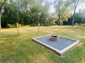 Relax in a serene outdoor space with a hammock and fire pit surrounded by lush greenery.