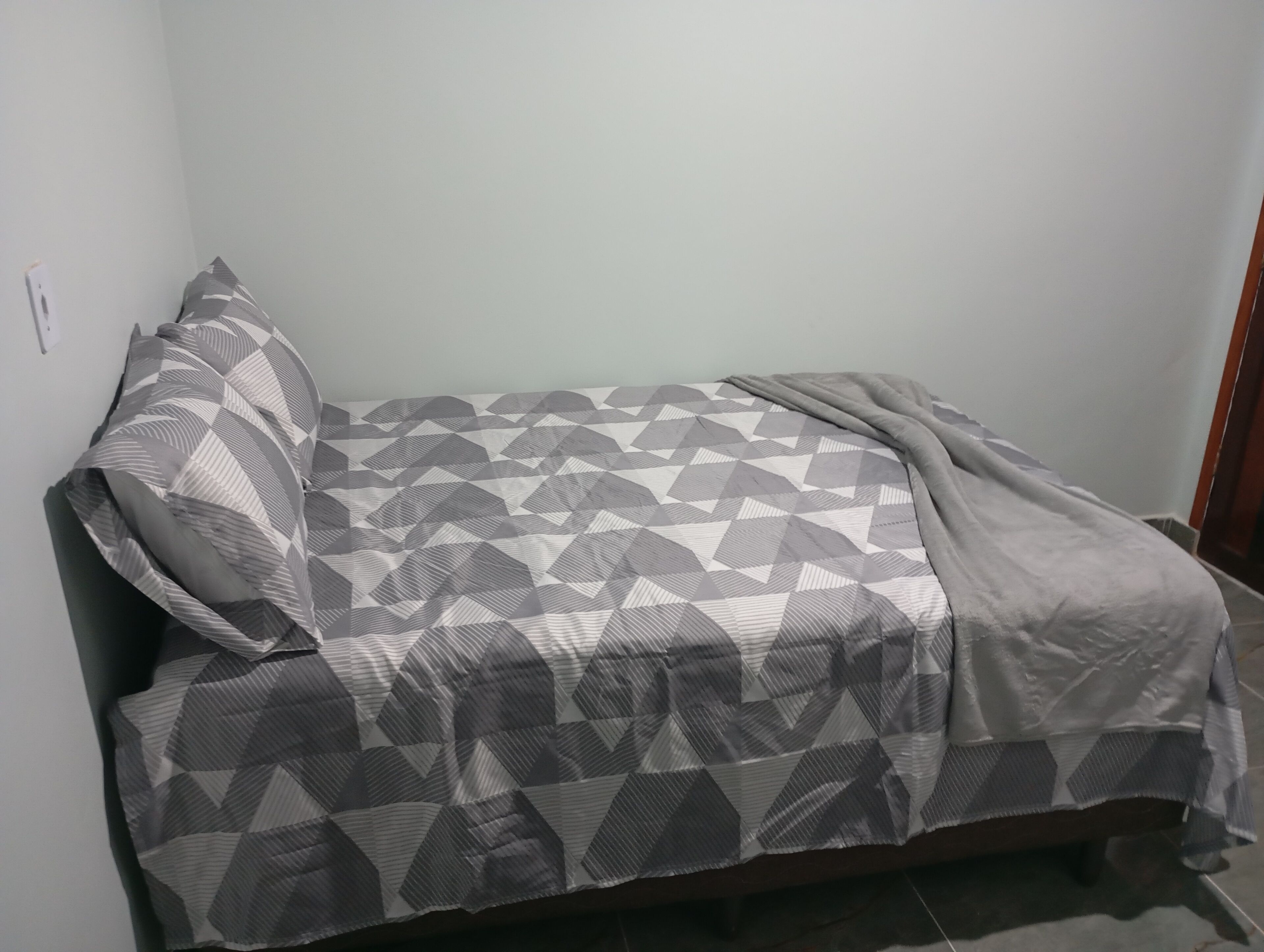 Una habitación pequeña con cama individual, una colcha de estampado geométrico y almohada a juego.