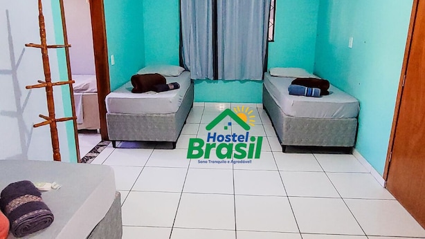 Una habitación pequeña con dos camas, una ventana con cortinas, una escalera de madera y piso de baldosas.