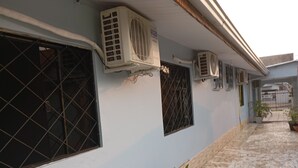 Un edificio con múltiples unidades de aire acondicionado instaladas en la pared exterior, un camino empedrado y plantas en macetas a lo largo del costado.