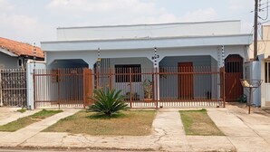 Una casa residencial con entrada protegida por un portón, un pequeño jardín y un camino de entrada pavimentado.