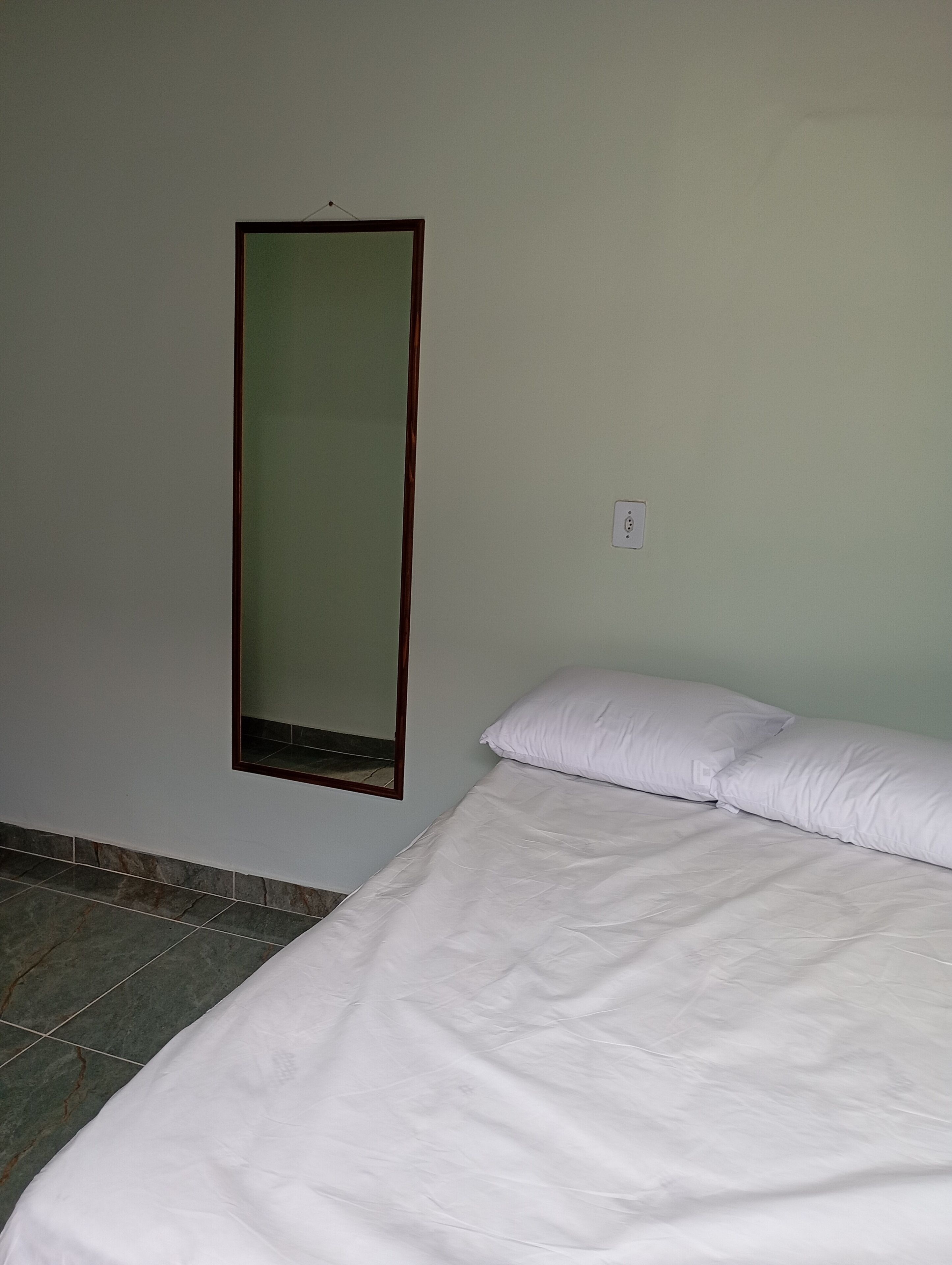 Una habitación con una cama, un espejo montado en la pared y un enchufe.